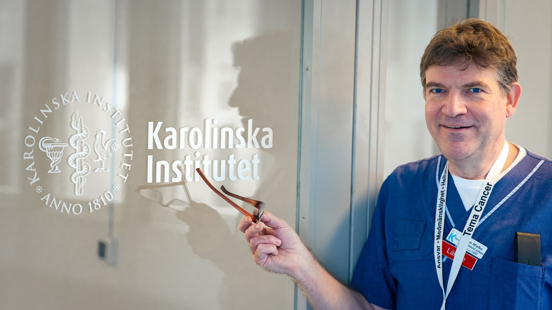 A man holding a pair of glasses in front of a sign of Karolinska Institutet.