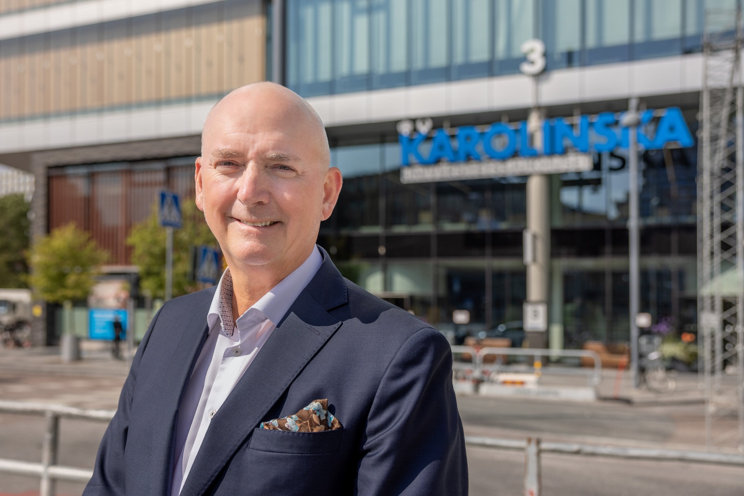 Sjukhusdirekt&ouml;r Christophe Pedroletti har m&ouml;rkbl&aring; kavaj, vit skjorta och en snusn&auml;sduk i kavajfickan. Han st&aring;r utanf&ouml;r huvudentr&eacute;n till sjukhuset i Solna.